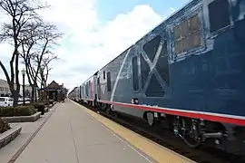 Two blue, red, and white diesel locomotives passing through a train station.