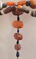 Four oval-shaped carnelian beads with guilloché pattern and one cylindrical bead with stepped pattern (top right) found in Susa excavations, Akkadian Empire or Ur III period. The carnelian is most probably from the Indus region, but the designs are typically Near-Eastern.