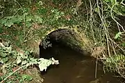 A small stream emerges from a brick culvert.