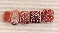 Indian carnelian beads with white design, etched in white with an acid, imported to Susa in 2600–1700 BCE. Found in the tell of the Susa acropolis. Louvre Museum, reference Sb 17751. These beads are identical with beads found in the Indus Civilization site of Dholavira.