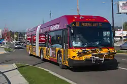 A red-and-yellow articulated bus seen on a suburban street from a nearby sidewalk. The bus's front sign reads "[A] Federal Way TC".