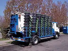 A truck similar in style to a garbage truck totes approximately 40 bins of food collected from a number of large kitchens. If the truck is associated with a company, the logo is not visible.