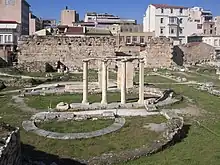 Photograph of Ancient Greek ruins, with modern buildings behind.