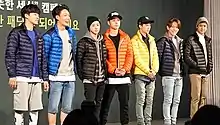  Seven men standing in line against a black wall