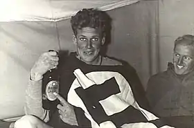 Wilfred Arthur holding a bottle of beer and grinning at the camera, in company with another grinning serviceman