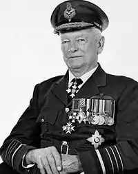 Half-portrait of uniformed man in peaked cap, wearing pilot's wings and a row of medals on left-breast pocket, plus three other star-shaped decorations