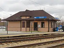 A pink-beige simple Tudor-style building seen from across two lanes of tracks, presumably the other platform of the station.