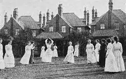 A group of 15 women in long-sleeved shirts and ankle-length skirts on a grass netball court