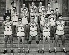 Three rows of five young men in white basketball uniforms stand on stone steps.