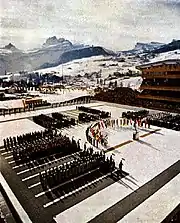 An open-air arena with crowds in the stands and people on the playing field surrounding a rostrum