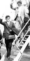 Two men in tuxedos are climbing down the stairs from an airplane