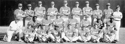 A black and white photograph of baseball players in uniforms and caps posed in three rows standing, sitting, and kneeing on a baseball field