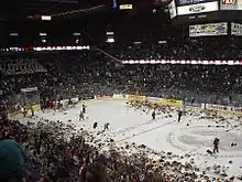 Wide angle shot of a hockey rink.  Fans on all sides are throwing stuffed animals onto the ice where several hundred are piling up.