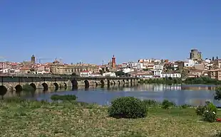 Photo of an arched stone bridge crossing a wide river with a city on the far bank