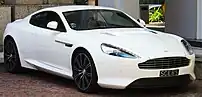 A vibrant front three-quarters view of a white 2013 facelift DB9 with a Singaporean vehicle registration plate.