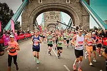 Selection of runners running towards the camera, with a stone bridge containing blue handles in the background.