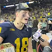 A football player talking to microphones on a football field.