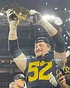 A smiling football player lifts a trophy