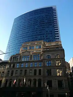 Ground-level view of a modern, 33-story skyscraper with a curved front and glass facade reflecting the blue of the sky