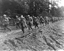 Two columns of Japanese American soldiers in route step in France.