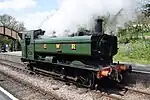 A green pannier tank locomotive blowing off steam as it moves backwards.