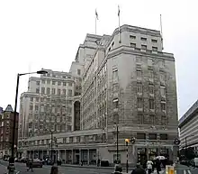 A large grey stone building rising to 13 floors topped with three flag poles