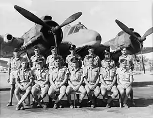 Formal portrait of six rows of men military uniforms, seated or standing in front of a building