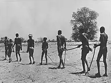 Black and white photo of children leading a line of adults across a dry landscape