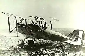 Side view of military biplane with pilot in cockpit, parked on an airfield