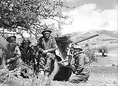 Four soldiers, dressed warmly with three of them wearing steel helmets, in front of a 2-pounder anti tank gun