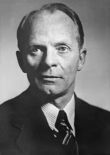 An en face black-and-white photo of a man in a suit with a tie