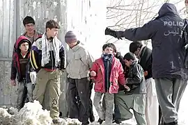 A member of the Afghan National Police trying to control local children awaiting the distribution of goods from the U.S. military for the winter months.