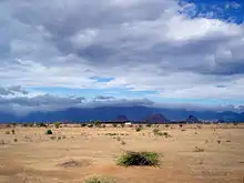 Desert under mostly cloudy sky, with hills in background