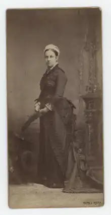 A black and white photograph of a woman in a dark dress standing in profile at an easel.