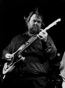 A black and white photo of musician Al Anderson, playing an electric guitar