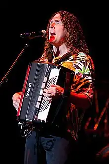 A man holding an accordion whilst singing into a microphone.