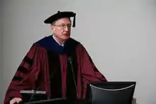 Middle-aged, bespectacled man in academic dress making a presentation