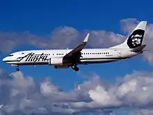 Left side view of an aircraft on final approach, with partly cloudy skies in the background.