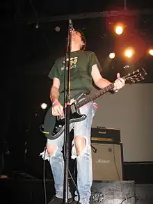 A man playing guitar on-stage and singing into a microphone