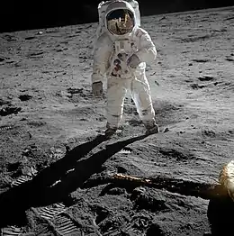 Aldrin stands on the Moon. Armstrong and the Lunar Module Eagle are reflected in his visor.