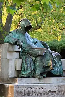 A man wearing a cowl which covers his face sits on a bench