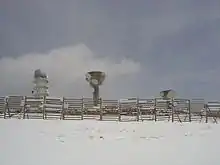 Three concrete radio towers with a fence between them and the camera