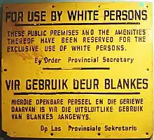 A sign with text in English and Afrikaans. The English text reads: "For Use By White Persons. These public premises and the amenities thereof have been reserved for the exclusive use of white persons. By Order Provincial Secretary".