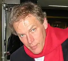 A man with short blond hair and blue eyes wearing a red scarf