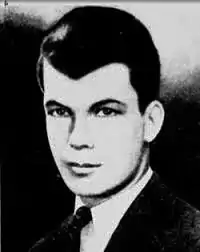 A black and white photo of a young man with well-coiffed dark hair wearing a jacket and tie