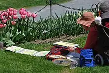 A woman in a large hat is doing a watercolor painting of pink tulips in front of her.