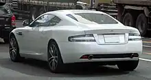 Rear three-quarters view of a white DB9 parked. It features clear white glass tail-lights.