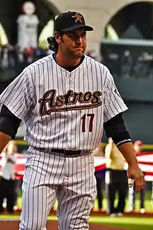 A man in a white baseball uniform with black pinstripes and cap