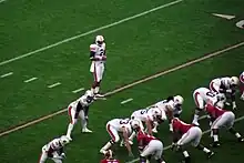 A quarterback is behind the offensive line preparing to take a snap.