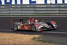 An Audi R10 at the Circuit de la Sarthe for the 2007 24 Hours of Le Mans, same as the previous cars, and has a German flag and is instead emblazoned with the number 1. Emanuele Pirro is at the wheel and is turning right.